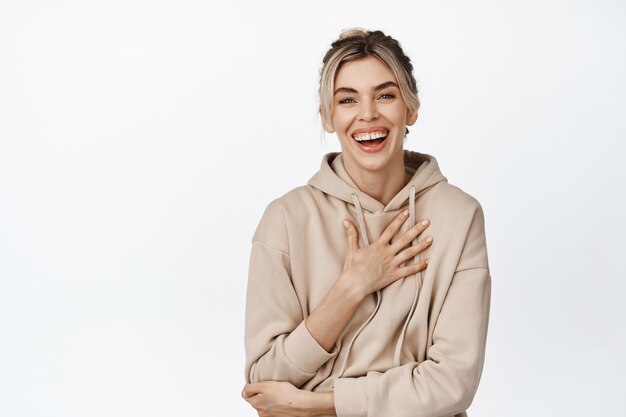 Young natural girl with white healthy smile, laughing and looking happy, standing in beige hoodie on white.