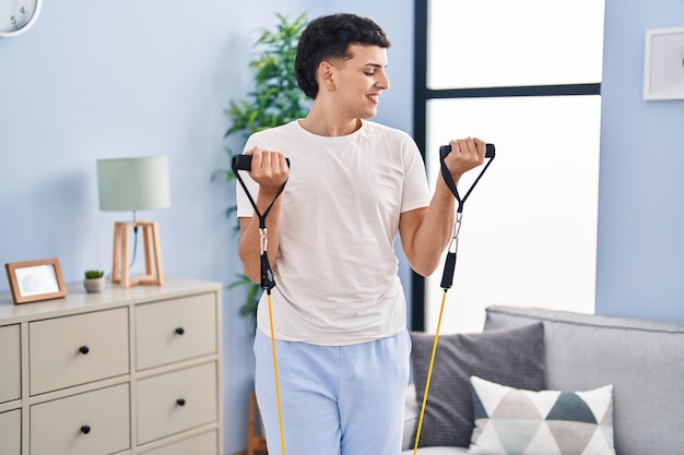 Free photo young non binary man smiling confident using elastic band training at home