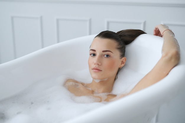 Молодая обнаженная женщина принимает расслабляющую пенную ванну
