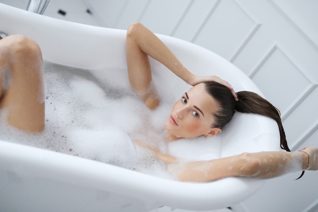 Молодая обнаженная женщина принимает расслабляющую пенную ванну