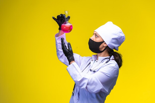 Young nurse in face and hand mask follows the reaction in flask and gets surprized. 