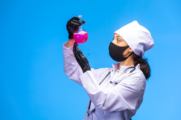 フェイスマスクとハンドマスクを着用した若い看護師がテストフラスコを持ち、化学反応を追跡します。