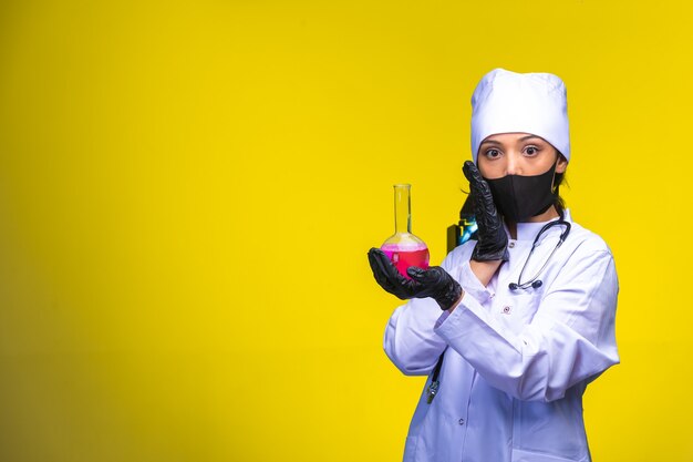 Young nurse in face and hand mask holds a test flask. 