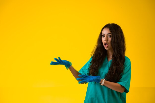 Young nurse in green uniform and plastic gloves making surprized face.