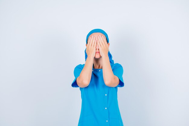 Young nurse is covering her eyes with hands on white background