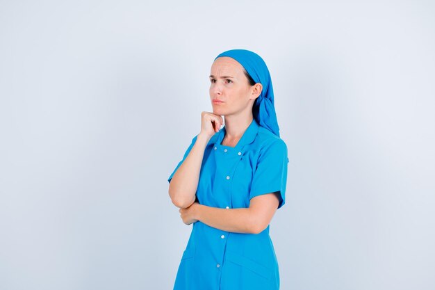 Young nurse is looking up by putting fist under chin on white background