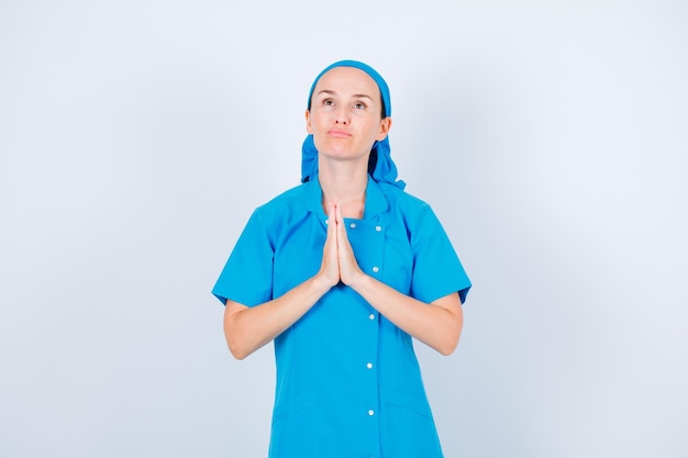 Free photo young nurse is praying by looking up and holding hands together on chest on white background