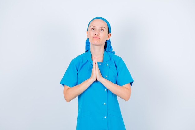 Young nurse is praying by looking up and holding hands together on chest on white background