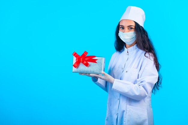 Young nurse in isolated uniform holding a gift box and presenting it. 