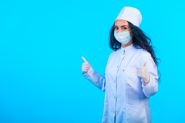 Молодая медсестра в изолированном холдинге униформы, делая знак руки вверх.