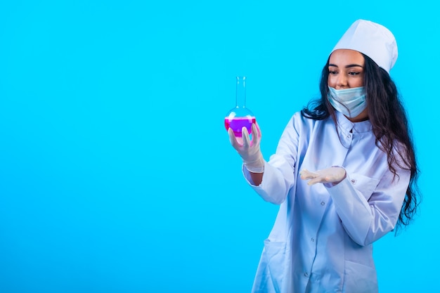 Young nurse in isolated uniform holding a test flask on blue wall.