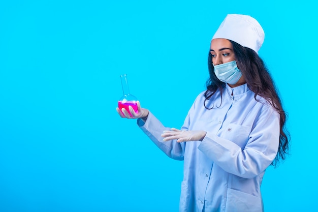 Young nurse in isolated uniform holding a test flask and describing it. 