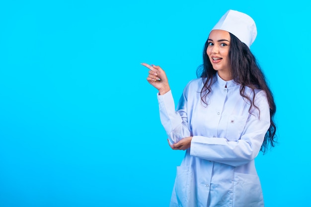 Young nurse in isolated uniform looks cheerful and points at something.