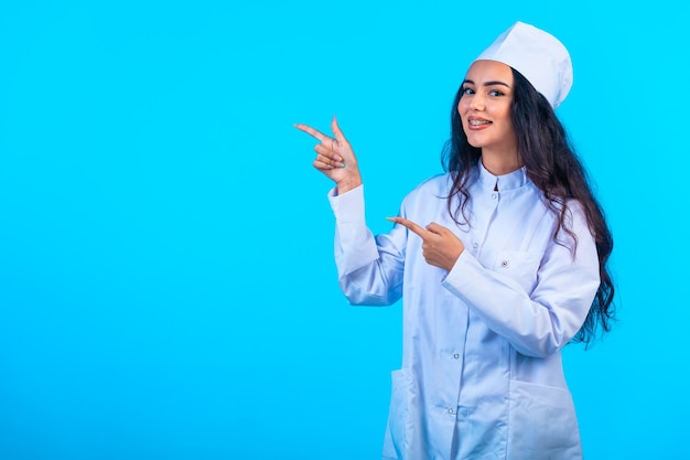 Young nurse in isolated uniform looks cheerful and points at something.