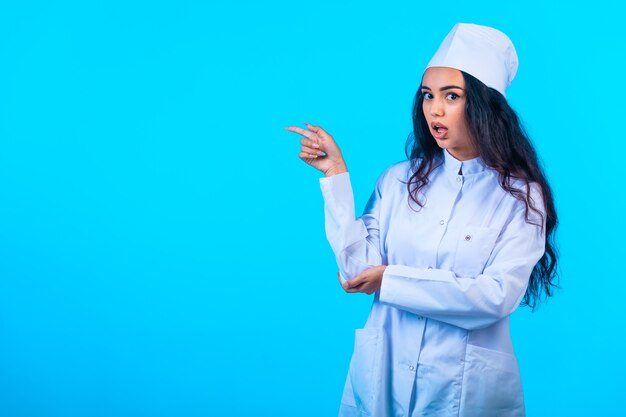 Young nurse in isolated uniform looks surprised and points at something