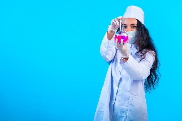 Молодая медсестра в изолированной униформе показывает химическую колбу