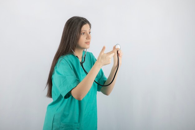 Young nurse looking at away and pointing finger to stethoscope.