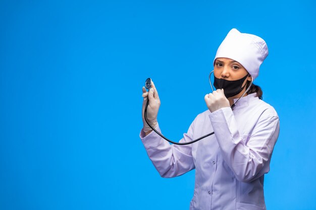 Young nurse in white uniform checks the patient with stethoscope, front view. 