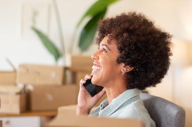 Young online shop worker calling client and smiling. Happy Black woman working in home office surrounded by cardboard parcels. Startup business, e-commerce concept