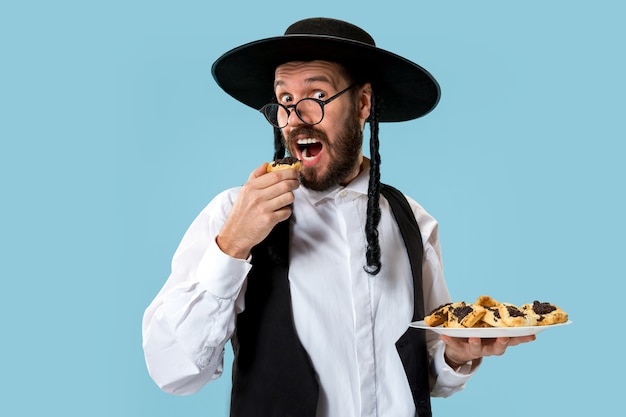 푸림의 유대인 축제를 위해 Hamantaschen 쿠키와 검은 모자를 쓴 젊은 정통 유대인 남자