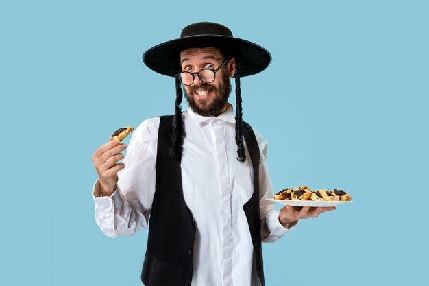 푸림의 유대인 축제를 위해 Hamantaschen 쿠키와 검은 모자를 쓴 젊은 정통 유대인 남자