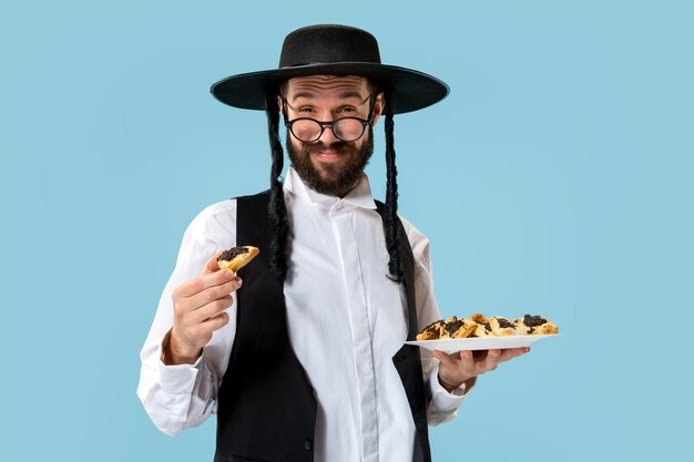축제 Purim을 위해 hamantaschen 쿠키를 가진 젊은 정통 유대인 남자. 휴일, 축하, 유대교, 과자, 전통, 쿠키, 종교 개념
