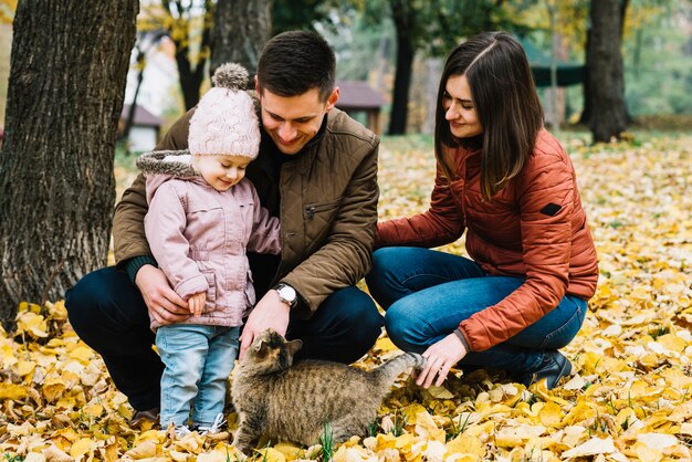 Молодые родители и маленький ребенок, играющий с кошкой в ​​Осеннем парке