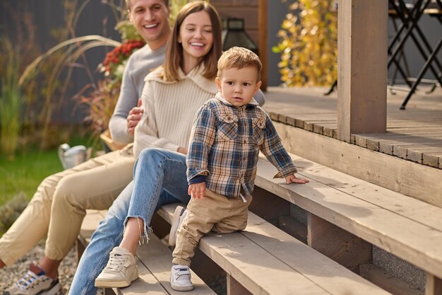 Young parents looking at little son sitting on porch