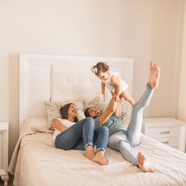 Young parents lying on bed and lifting daughter