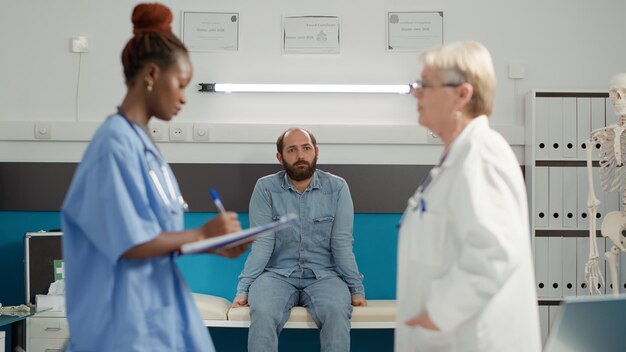 Young patient sitting in medical cabinet and waiting for exam results to find about disease diagnosis. Sick person attending consultation appointment with medical staff team in office.