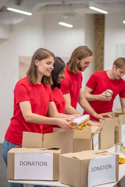 Young peeple in red packing the cardboards with humanitarian help