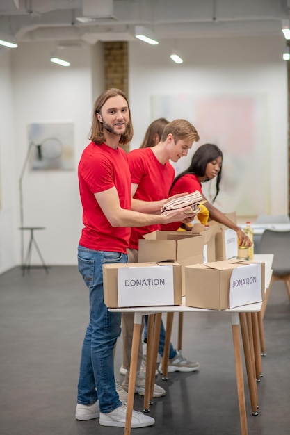 Young peeple in red packing the cardboards with humanitarian help