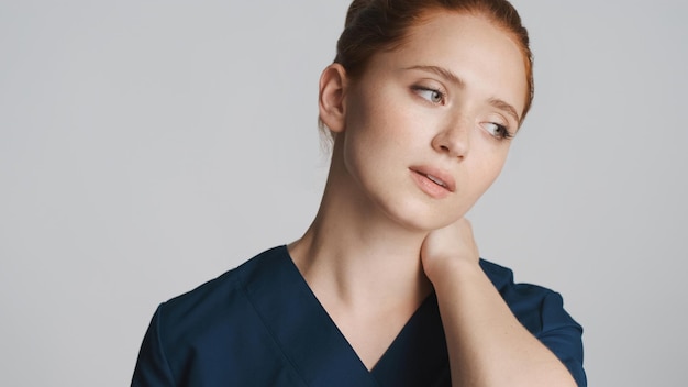 Молодая задумчивая женщина-врач устало смотрит в сторону на белом фоне Усталое выражение лица