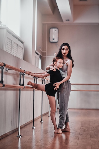 Молодая задумчивая девушка получила специальную репетицию балета от веселого прилежного тренера в светлом тренировочном зале.