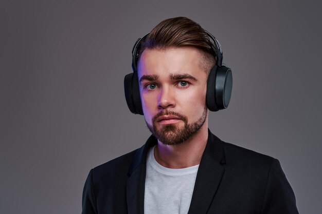 Young pensive man in wireless headphones is listening trendy music.