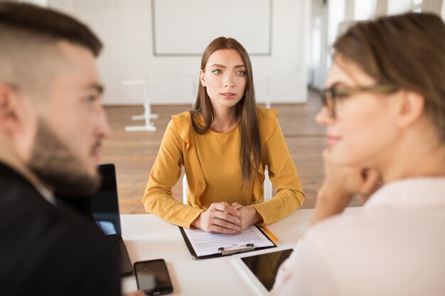 ブラウス姿の若い物思いにふける女性が、現代のオフィスで時間を過ごしながら、夢のように雇用主を見つめています。面接の結果を待っている女性志願者