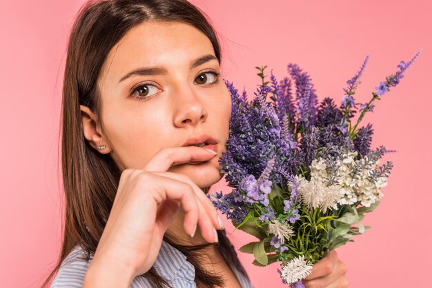 顔の近くの花の束を保持している物思いにふける若い女性