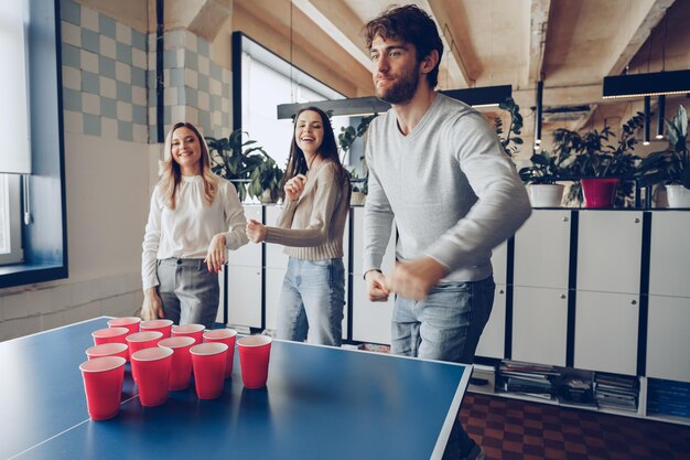 Young people coworkers playing beer pong in modern office