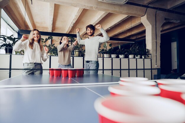 Young people coworkers playing beer pong in modern office