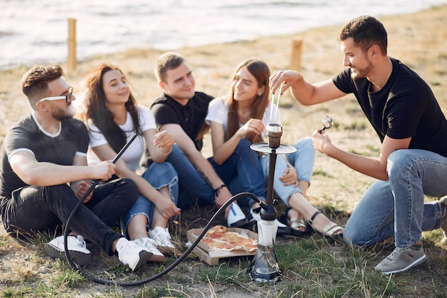 Young people eating pizza and smoking shisha at the beach