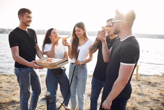 Молодые люди едят пиццу и курят кальян на пляже