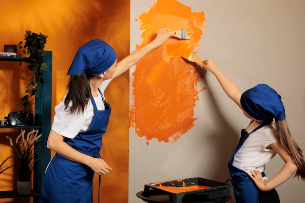 家のアパートの壁をオレンジ色に塗り、絵筆を使い、家事を改善するための道具を改造する若者たち。お母さんと女の子が家の部屋をカラーペイントとブラシで模様替え。