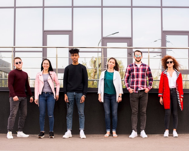 Free photo young people standing in a row in front of glass building