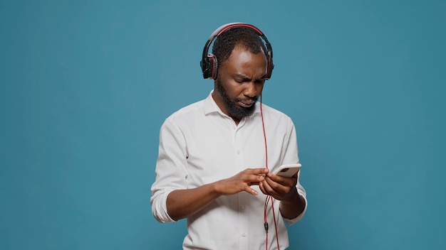 Young person listening to sound on headphones with mobile phone, paying attention to podcast. Confused man feeling uncertain about internet information on smartphone and audio heaset.