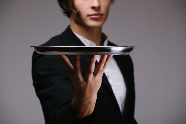 Young person in a suit holding an empty tray isolated on white wall