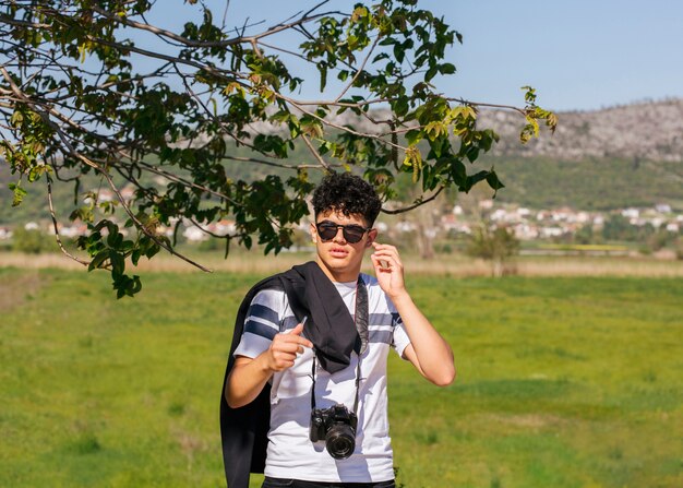 young photographer with camera standing on green landscape