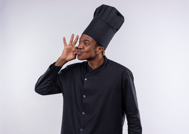 Young pleased afro-american cook in chef uniform gestures tasty delicious hand sign isolated on white wall 