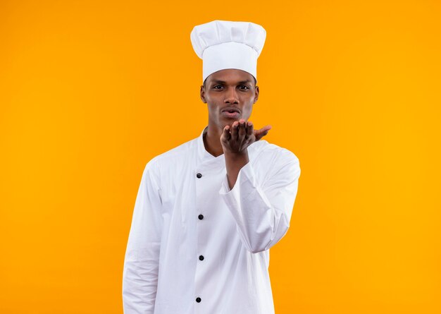 Young pleased afro-american cook in chef uniform sends kiss isolated on orange wall