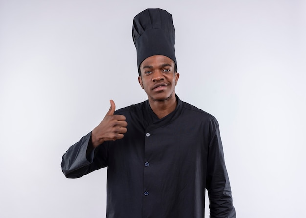 Молодой довольный афро-американский повар в униформе шеф-повара, пальцы вверх изолирован на белой стене