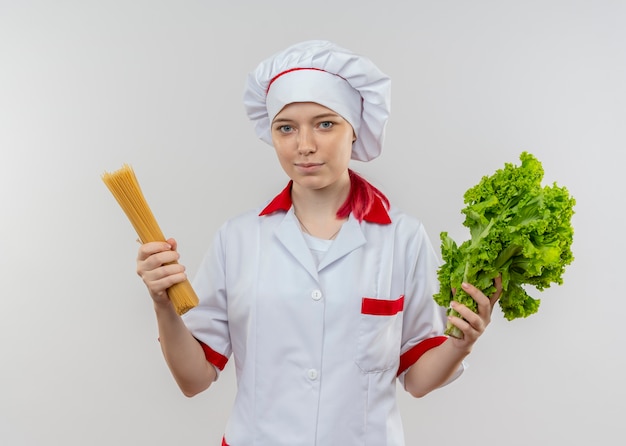 Il giovane chef femminile biondo felice in uniforme del cuoco unico tiene il mazzo di spaghetti e insalata isolati sulla parete bianca